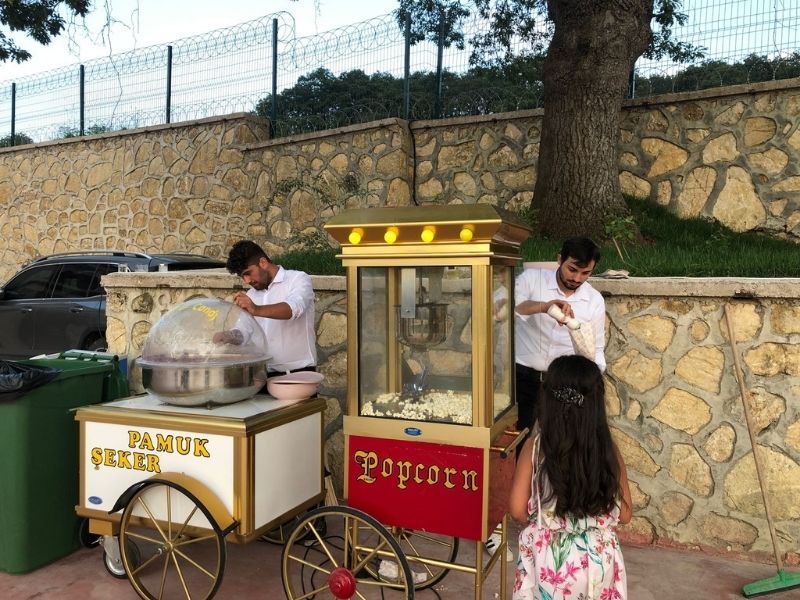 Düğün organizasyonunda çocuklar patlamış mısır arabası önünde neşeyle poz veriyor.